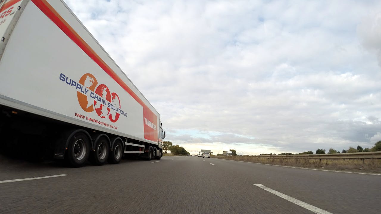 A large semi truck labeled 'Supply Chain Solutions' travels down a highway under a cloudy sky.